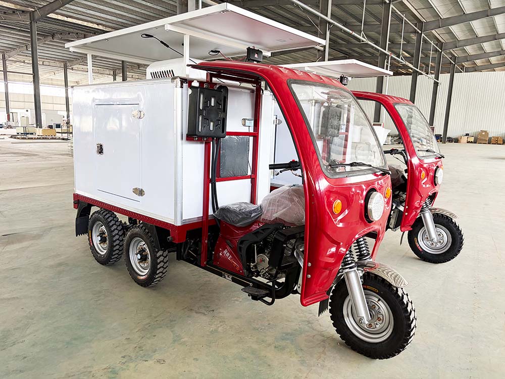 Two red refrigerated tricycles displayed on a factory floor